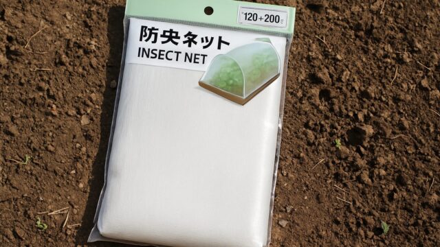 畑の土の上に置かれたダイソーの防虫ネット（パッケージ入り）の写真。背景には小さな芽が見える。