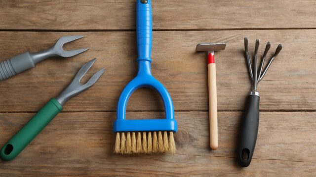 木製のテーブルの上に並べられた雑草ブラシと4つの園芸道具