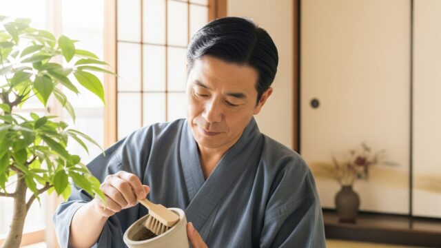 家庭環境で、【日本人】の人物がセメント鉢に入った植物の手入れをしており、小さなブラシで鉢を掃除しています。明るい環境です。