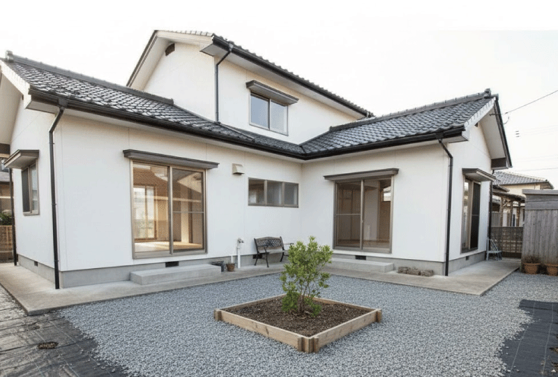 明るく親しみやすい写真スタイル。 防草シート＋砂利で仕上げたシンプルな住宅の庭。 コストを抑えた実用的な雰囲気。 日本の戸建て住宅、自然光。16:9。