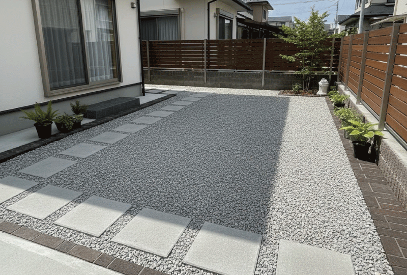 明るく親しみやすい写真スタイル。 建物の影になる庭スペースで、水たまりがなく乾いた地面。 砂利や透水性素材が使われている。 日本の戸建て住宅。