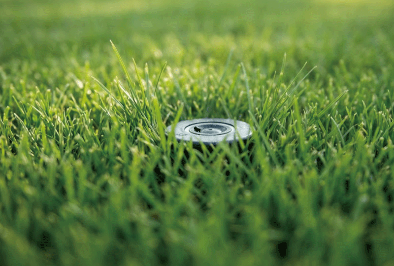 芝生の中に埋め込まれ、目立たないように収納されたポップアップ式スプリンクラーのヘッド。