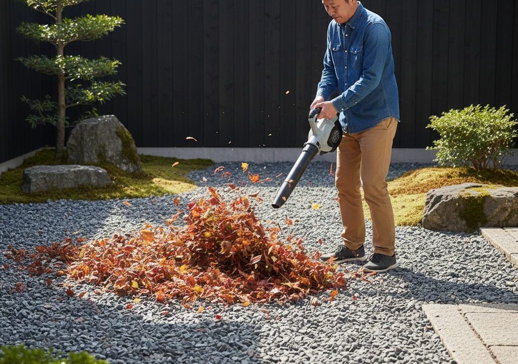 ブロワーを使って、砕石の上に落ちた枯れ葉を掃除している日本人の男性。