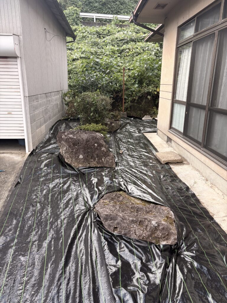 造園現場で庭石の形に合わせて黒い防草シートを施工した様子